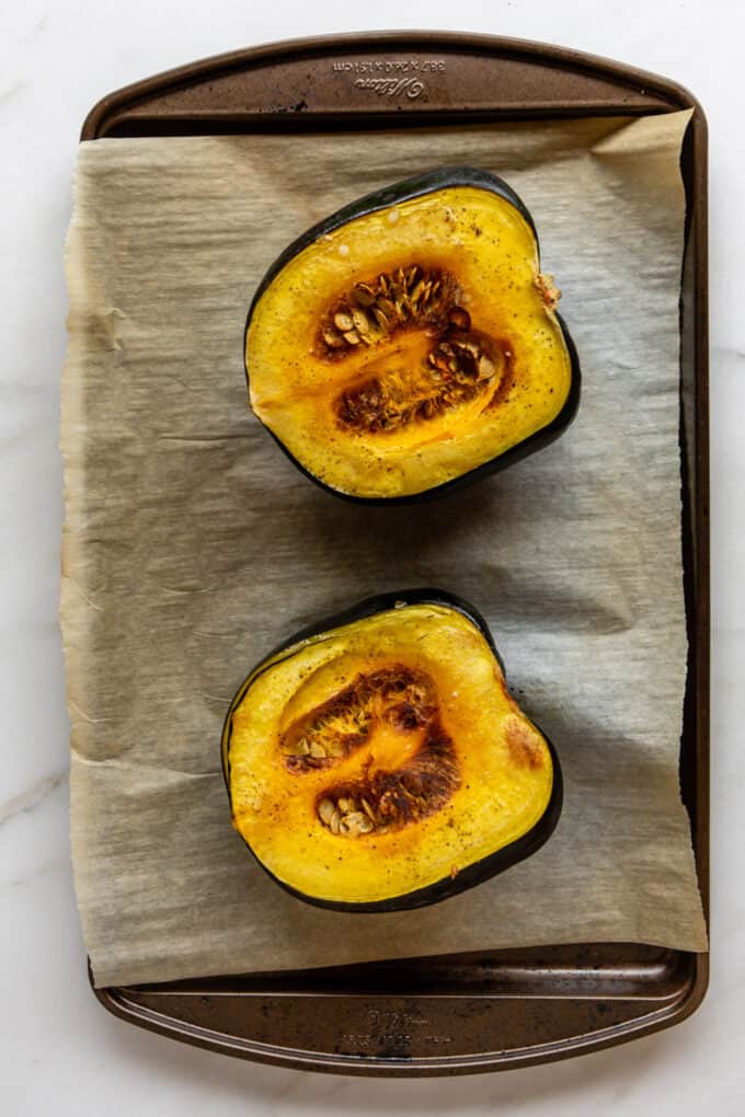 a roasted acorn squash cut in half on a baking tray