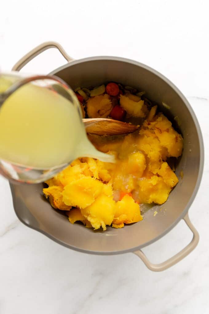 broth being poured into a large pot of acorn squash