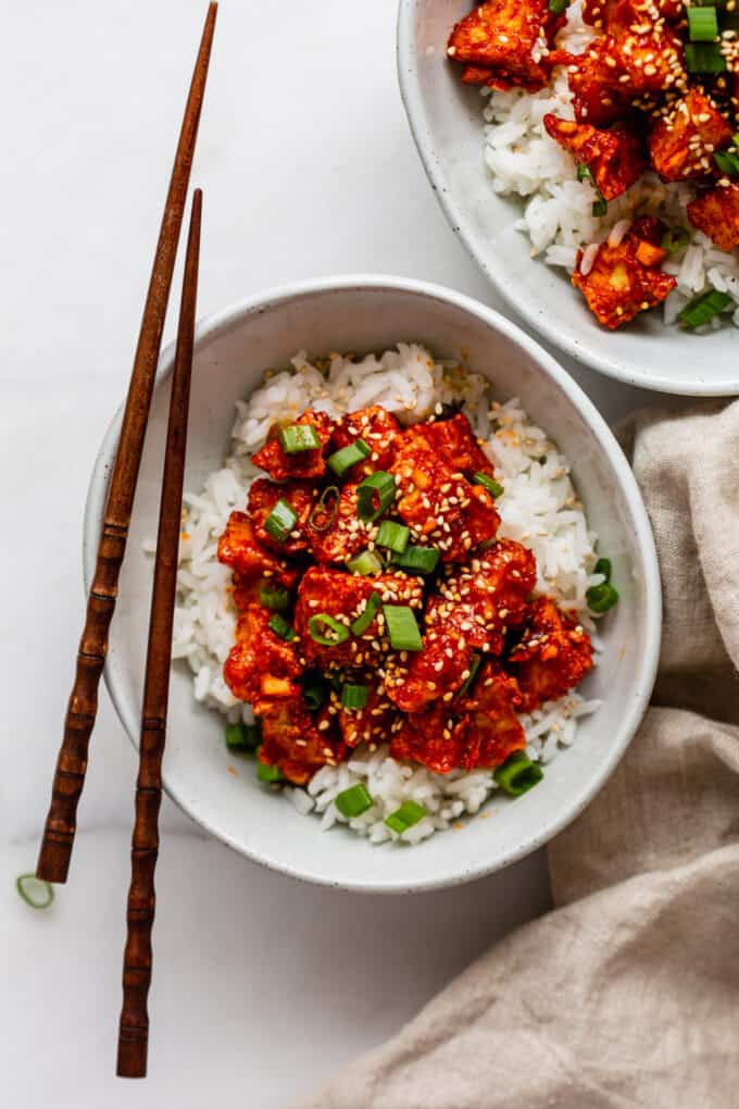 two bowls of gochujang Tofu with wood chopsticks and a beige napkin