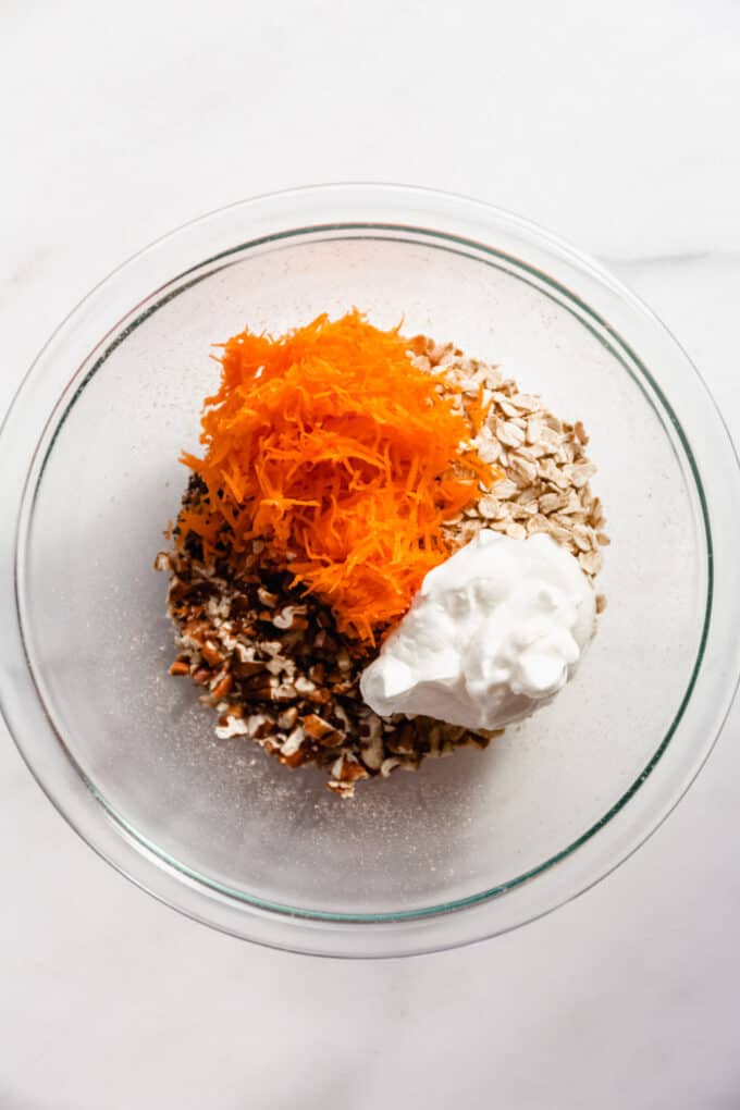 oats, walnuts, yogurt and shredded carrots in a clear mixing bowl