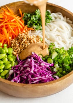 peanut sauce being poured into a bowl of Thai noodle salad