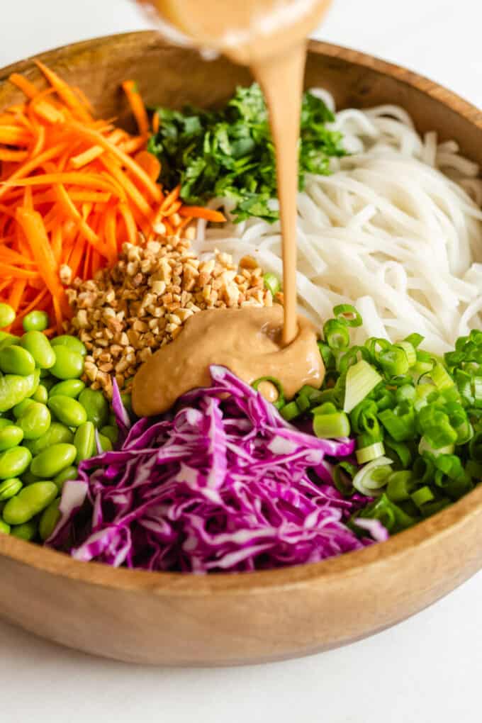 peanut sauce being poured into a bowl of Thai noodle salad