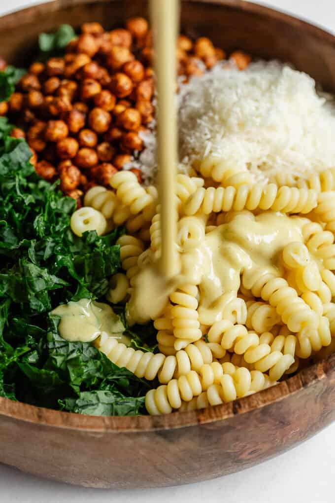 caesar dressing being poured into a bowl of pasta salad