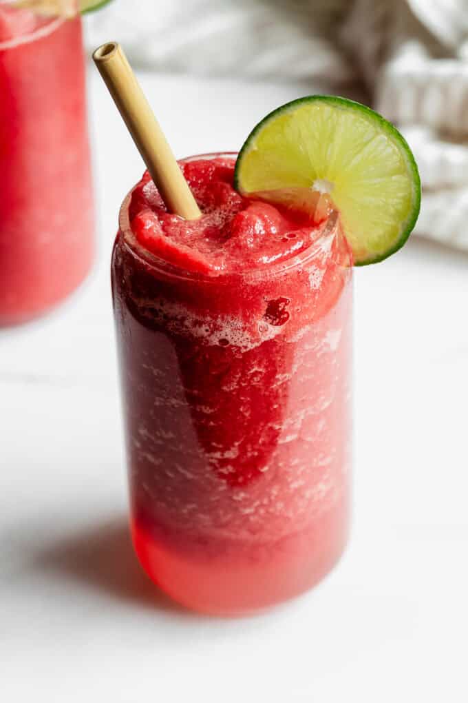 two glasses of watermelon slushies on a marble counter with a striped napkin