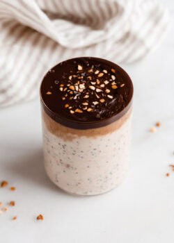 a cup of snickers overnight oats with a beige striped napkin in the back