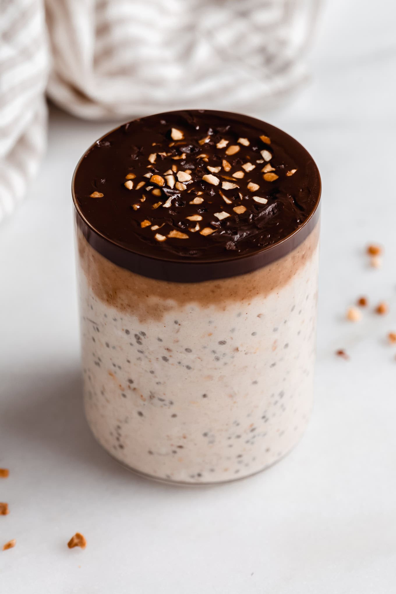 a cup of snickers overnight oats topped with chocolate and crushed peanuts.