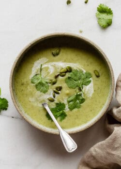 a bowl of broccoli cauliflower soup topped with cilantro and pumpkin seeds