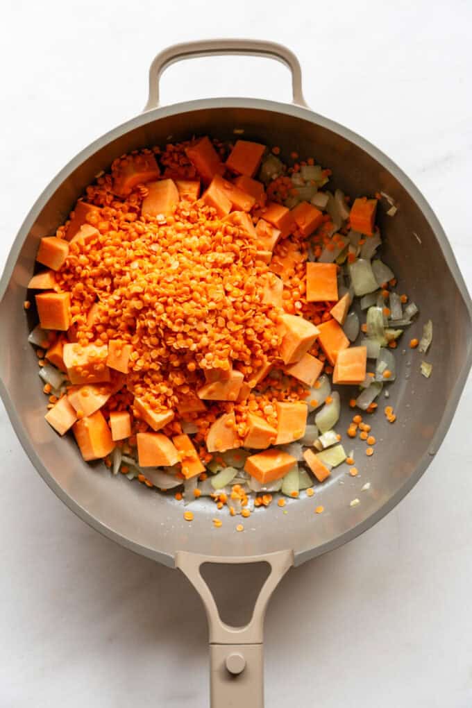 onions, cubed sweet potato and red lentils in a taupe pan
