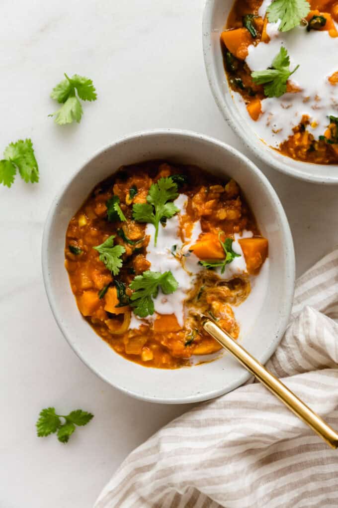 sweet potato lentil curry in a white bowl with a gold spoon
