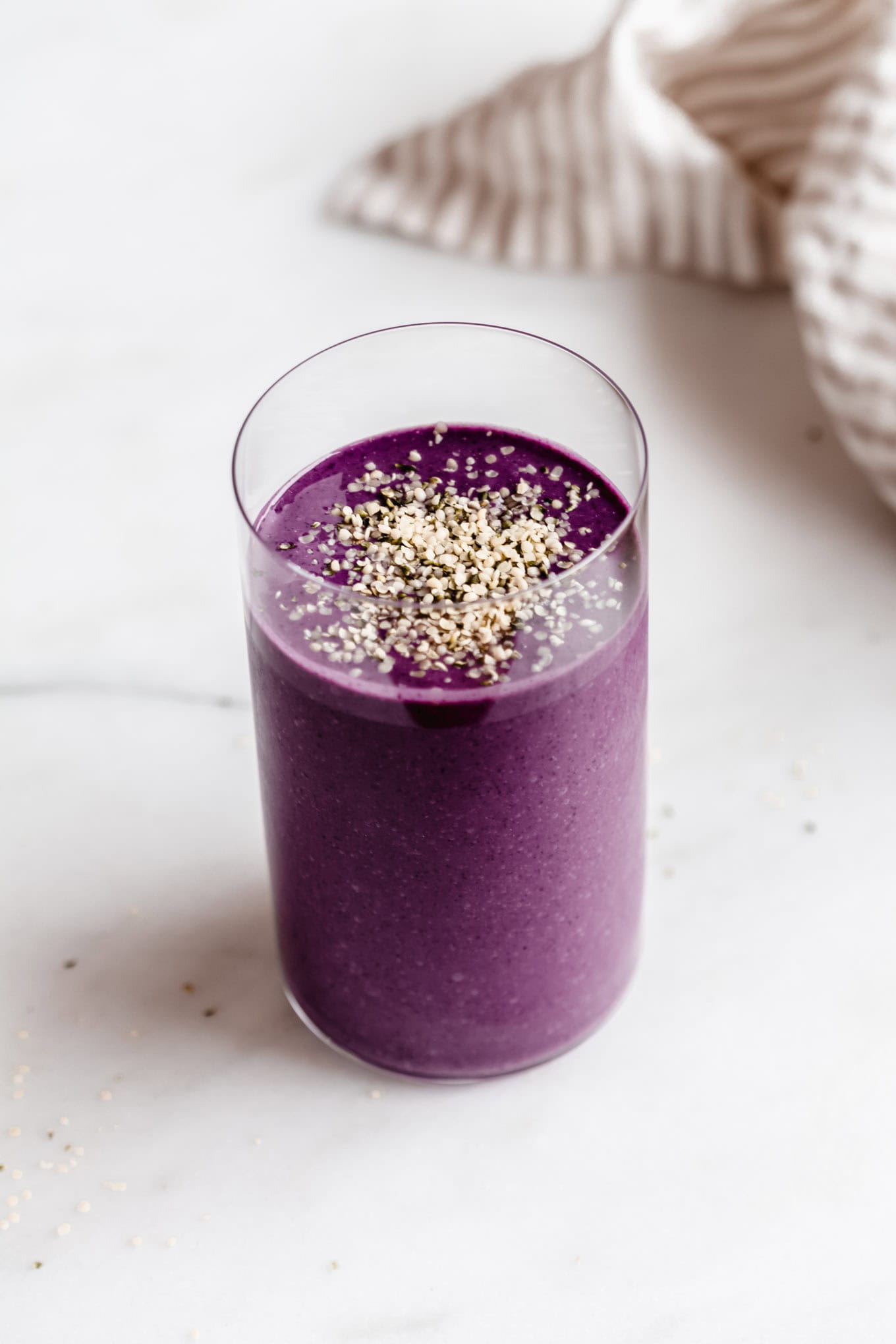Berry protein smoothie in a tall glass with a stripped napkin on the side