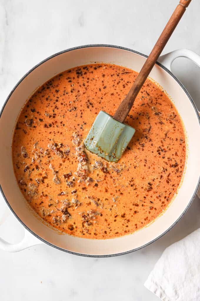 creamy sundried tomato sauce in a white pot with a spatula