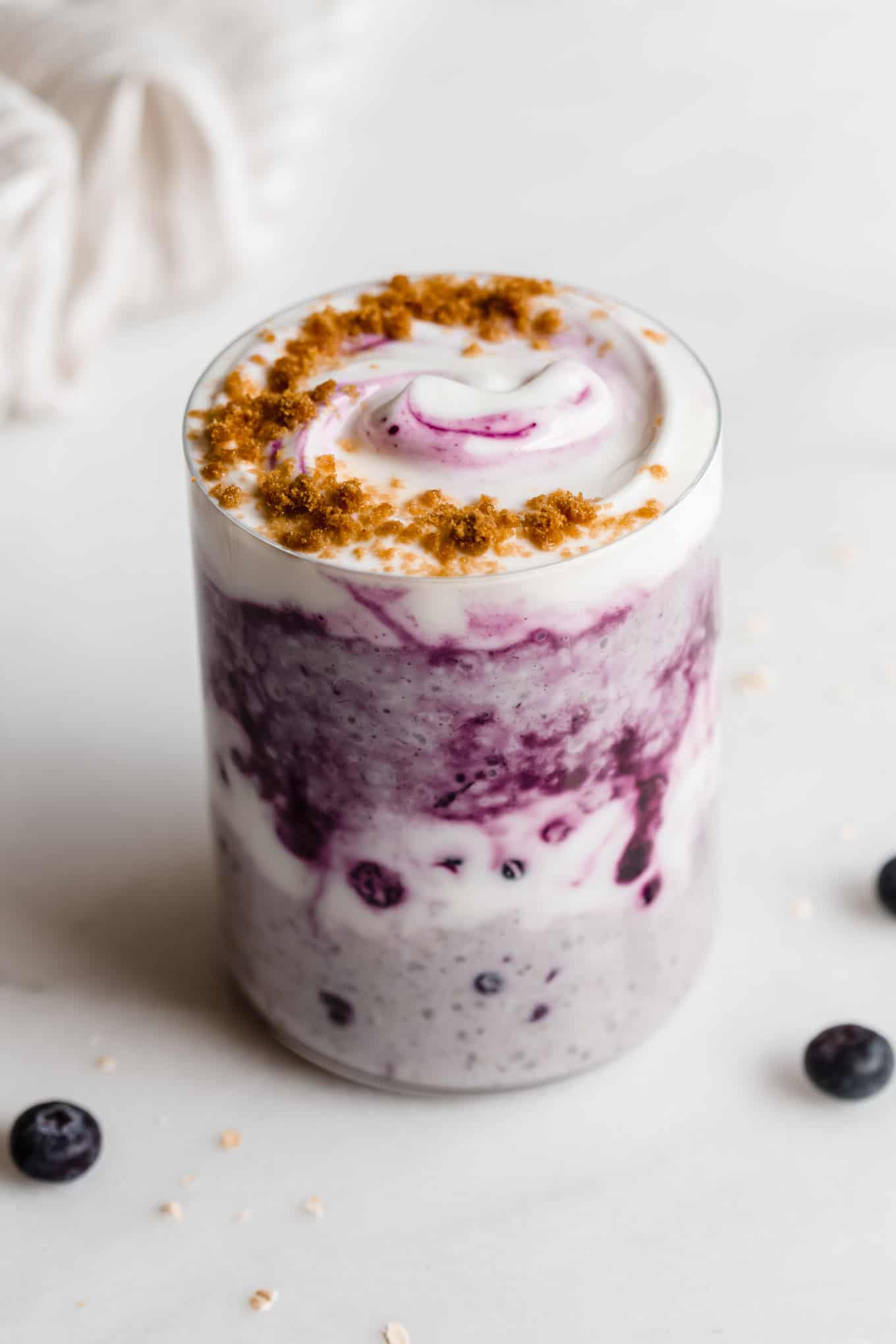 A cup of blueberry overnight oats topped with yogurt and crushed graham crackers.