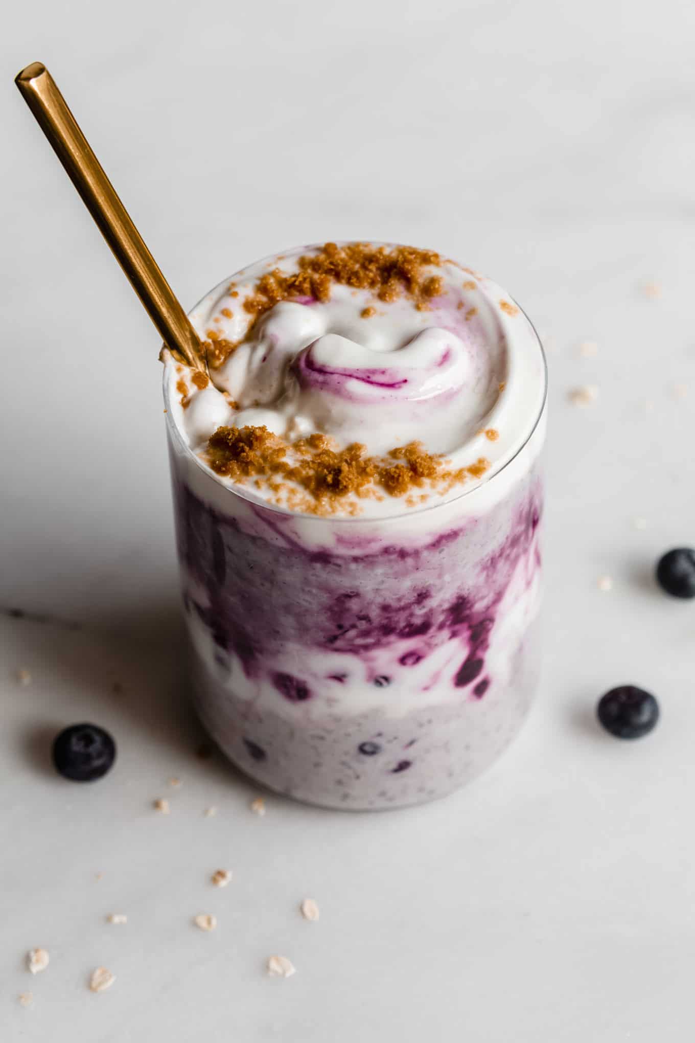 Blueberry overnight oats in a cup topped with yogurt with a gold spoon in it.