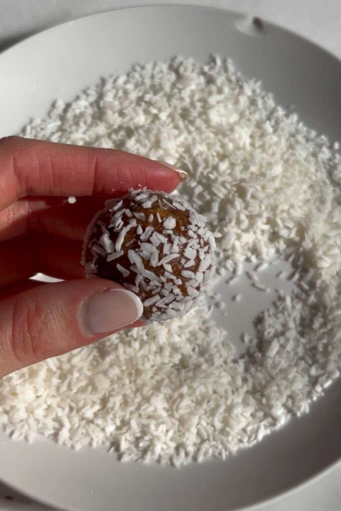 A carrot cake energy ball being rolled into shredded coconut