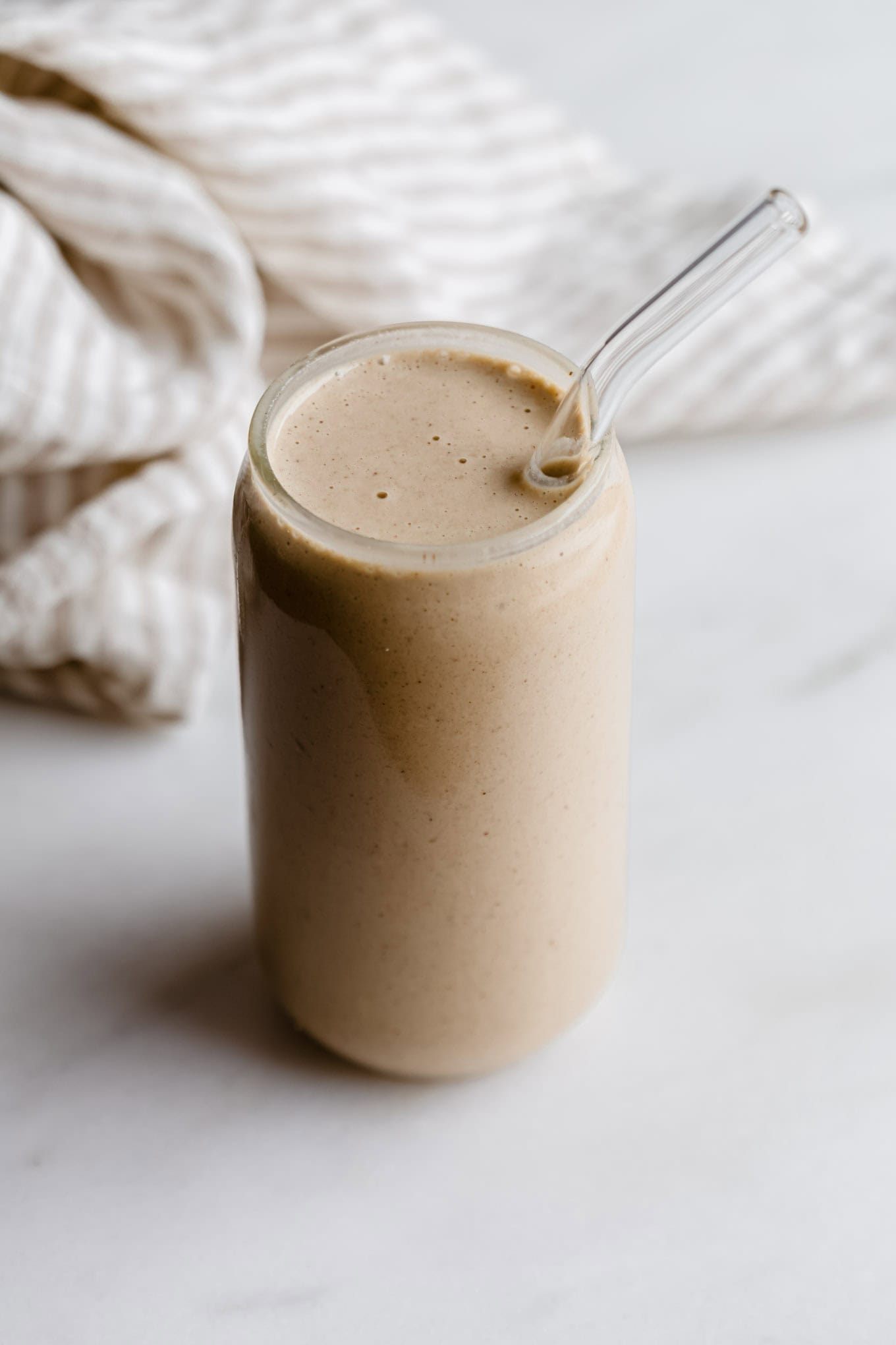 A banana date smoothie in a glass with a glass straw.