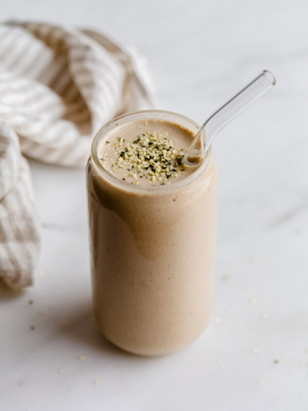 A banana date smoothie in a glass topped with hemp seeds and a striped beige napkin on the side.