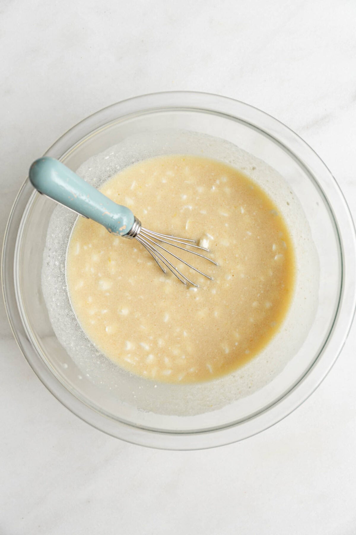 wet ingredients to make blueberry cottage cheese muffins mixed up in a mixing bowl with a blue whisk.