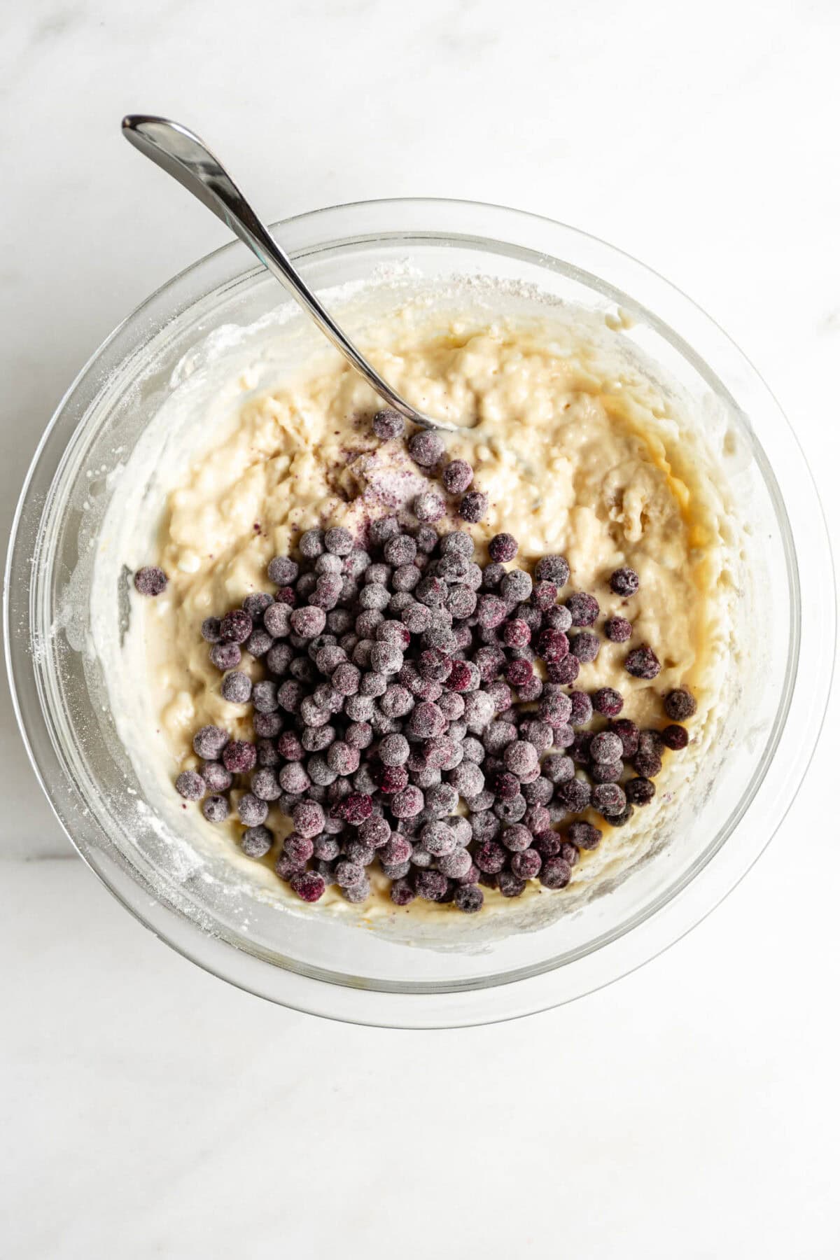 blueberry muffin batter with a pile of blueberries in a clear mixing bowl.
