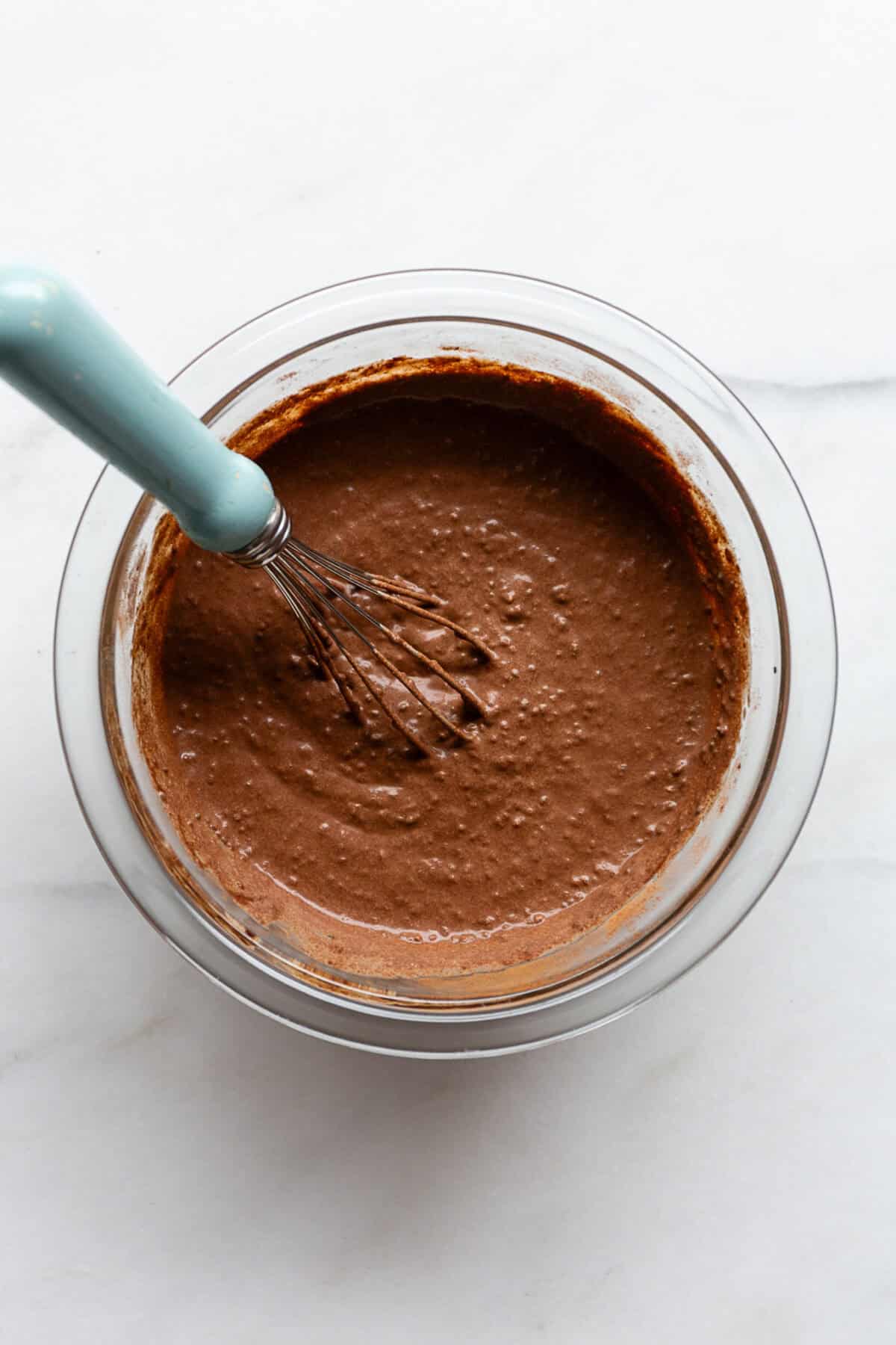 un-set chocolate chia pudding in a mixing bowl with a blue whisk.