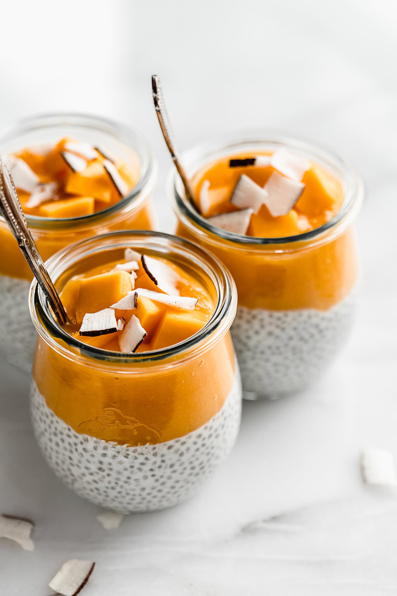 three cups of coconut chia pudding topped with mango puree.