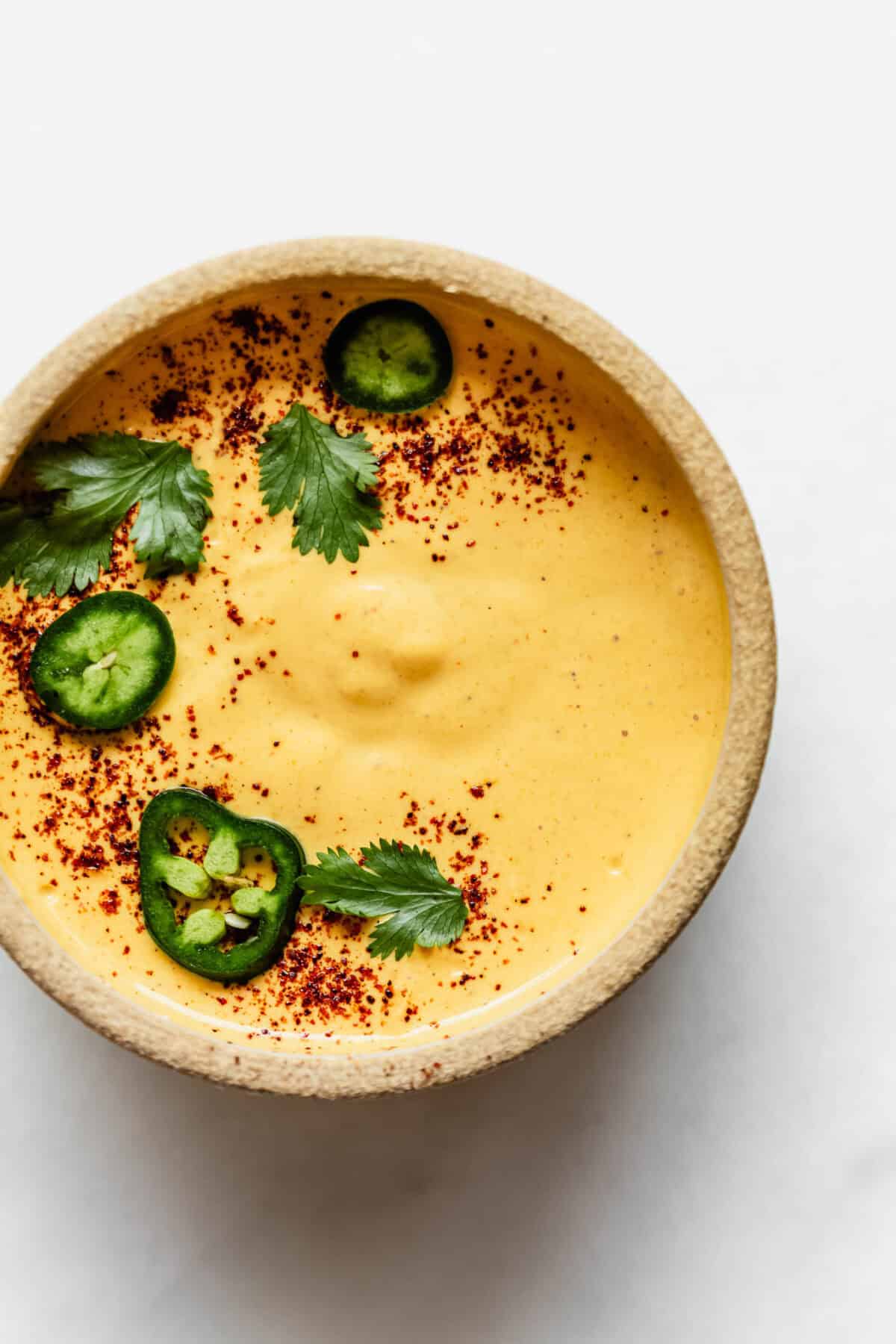 Cottage cheese queso in a bowl topped with sliced jalapenos and cilantro.