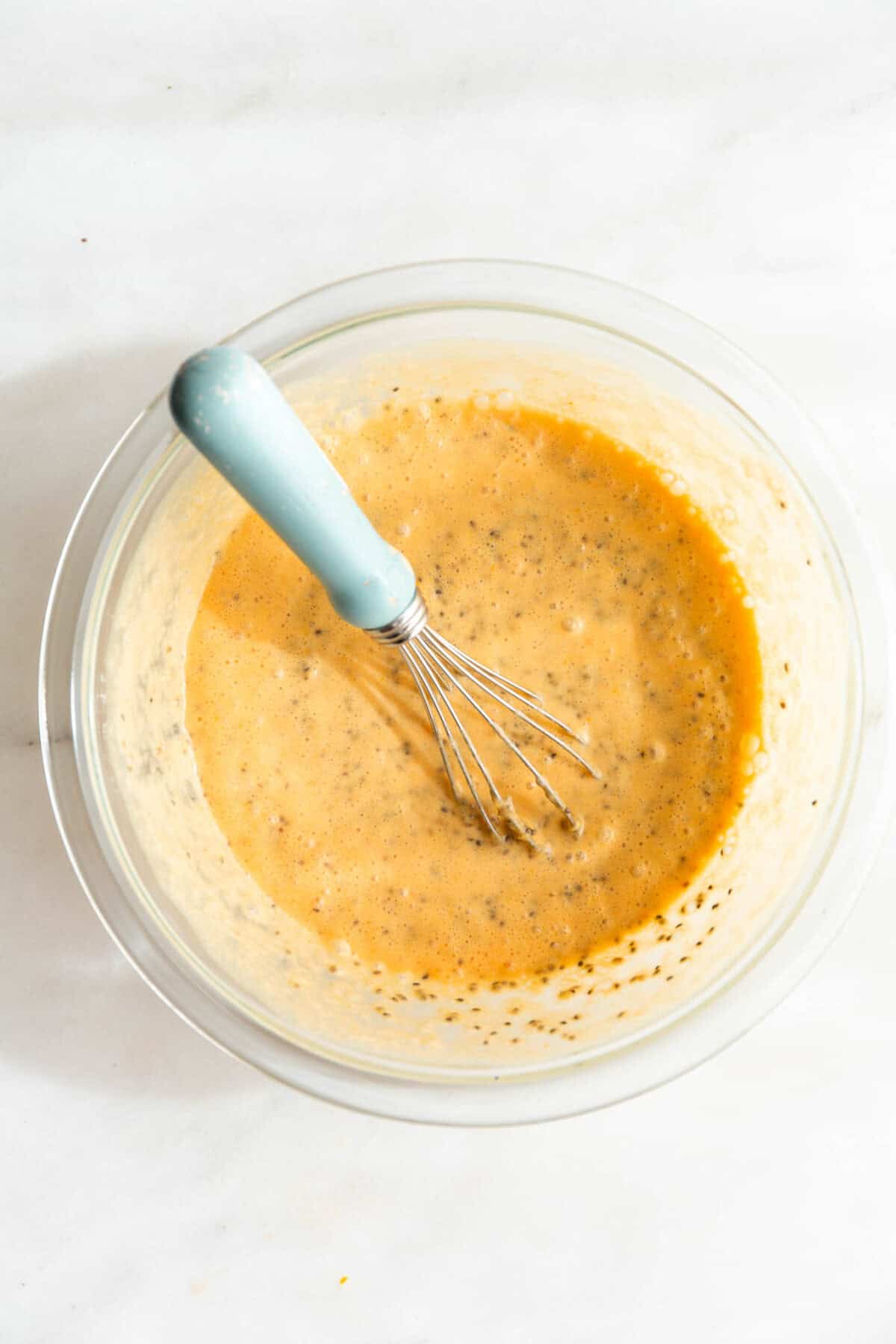 unset orange chia seed pudding in a mixing bowl with a blue whisk.