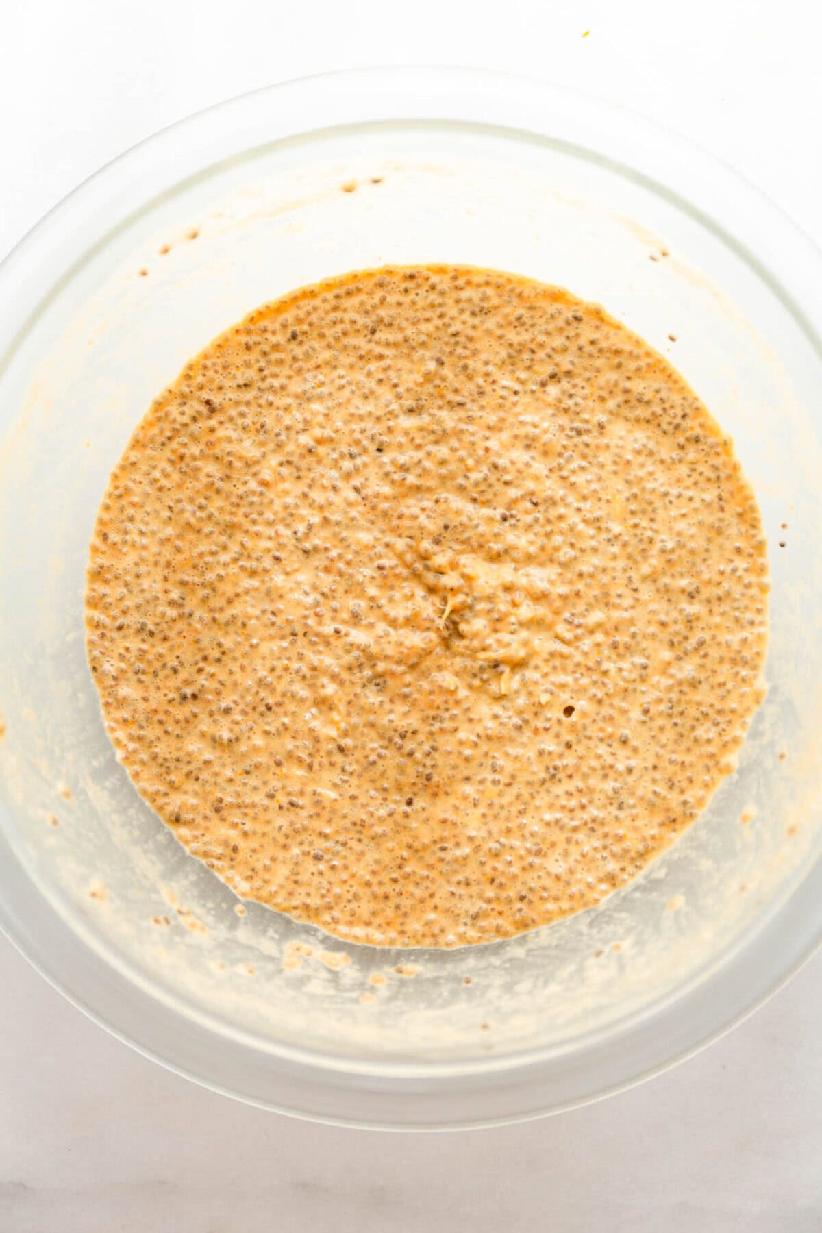 orange chia seed pudding in a clear mixing bowl.