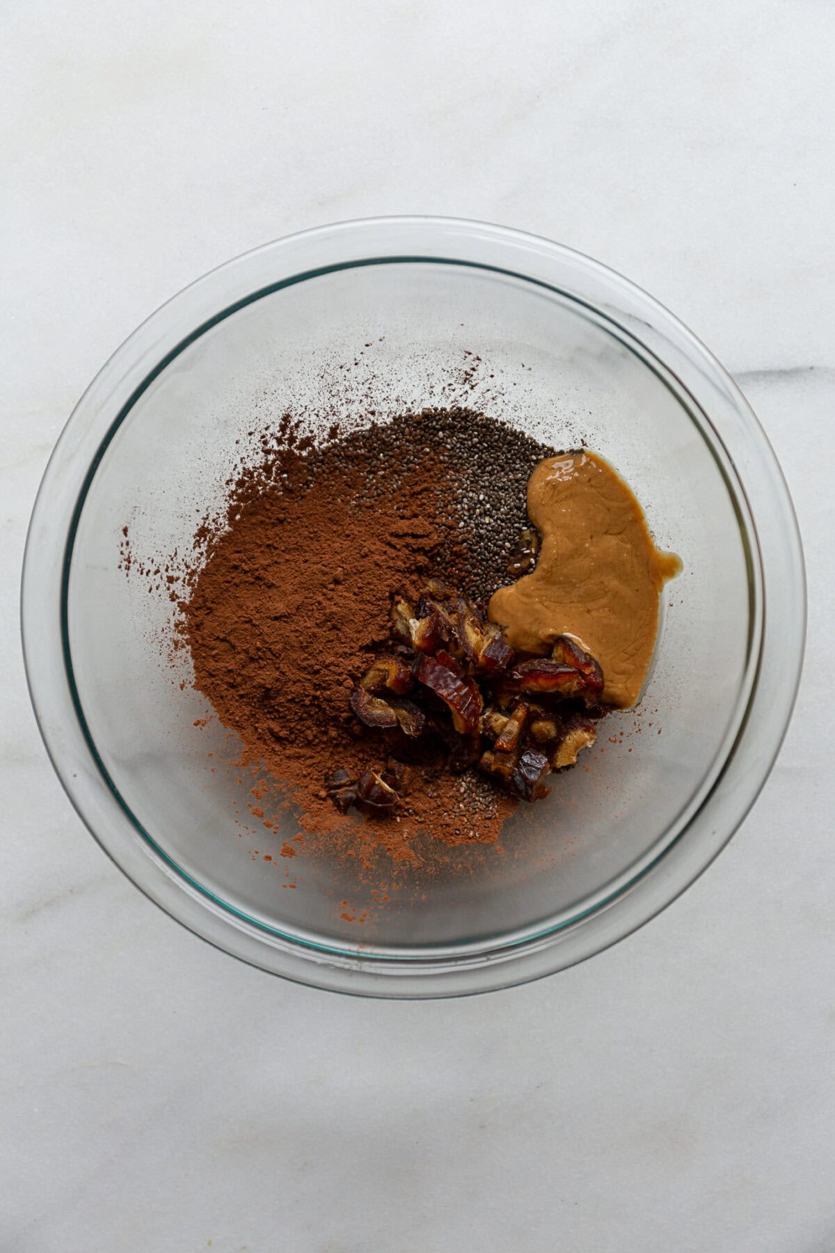 chia seeds, cocoa, peanut butter and dates in a clear mixing bowl.