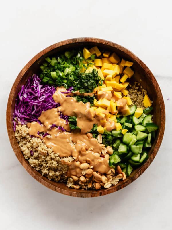 Thai quinoa salad in a wood salad bowl with peanut dressing poured over it.