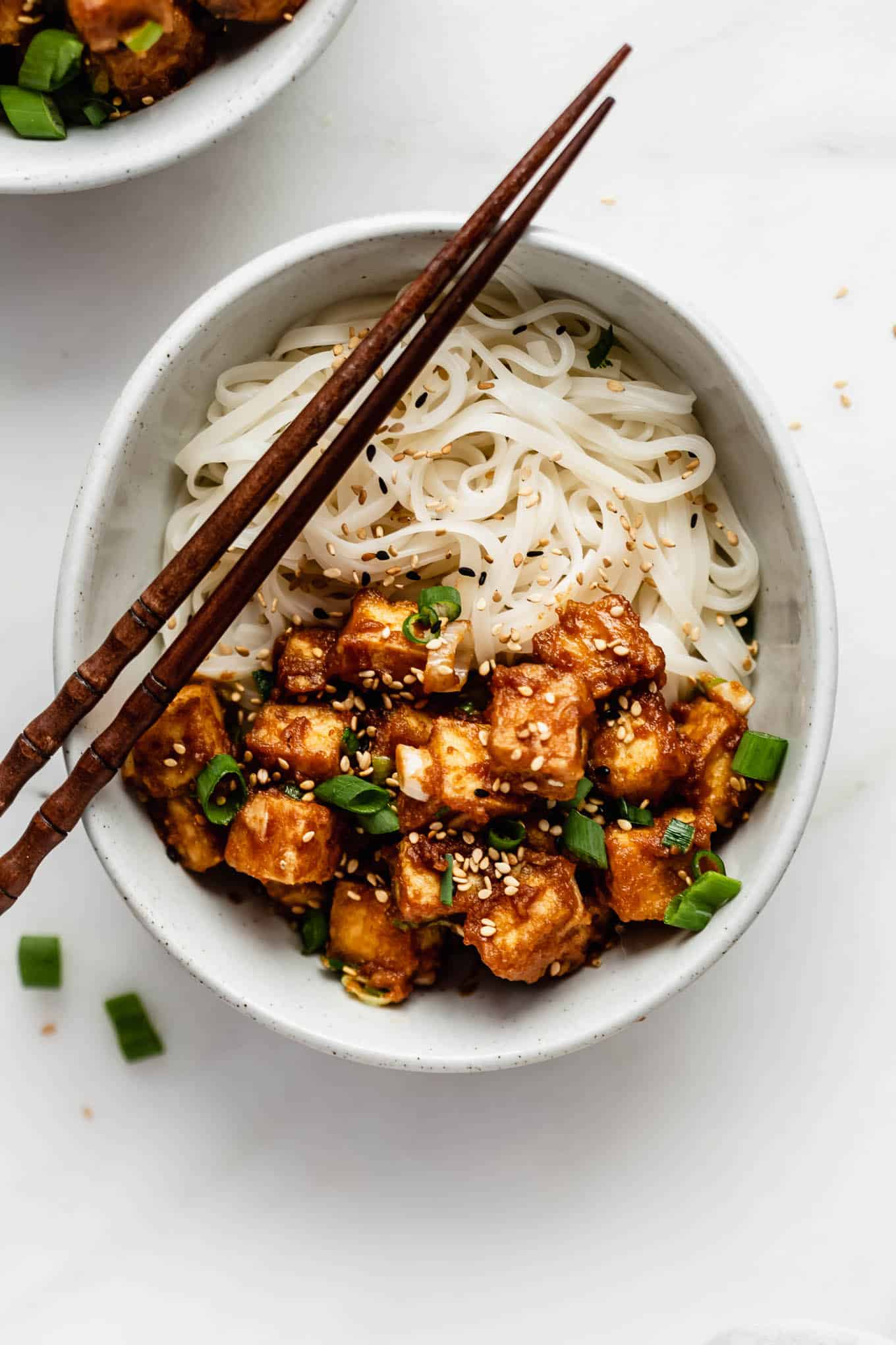 peanut butter tofu in a bowl with rice noodles and chopsticks.