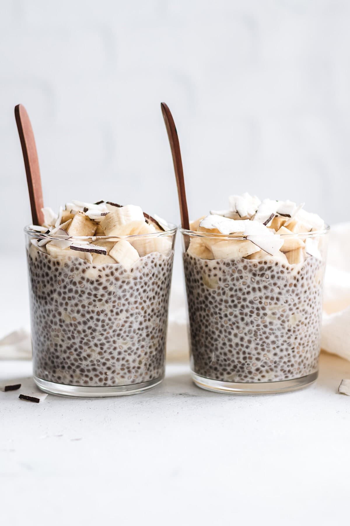 two cups of banana chia pudding topped with banana and coconut flakes.