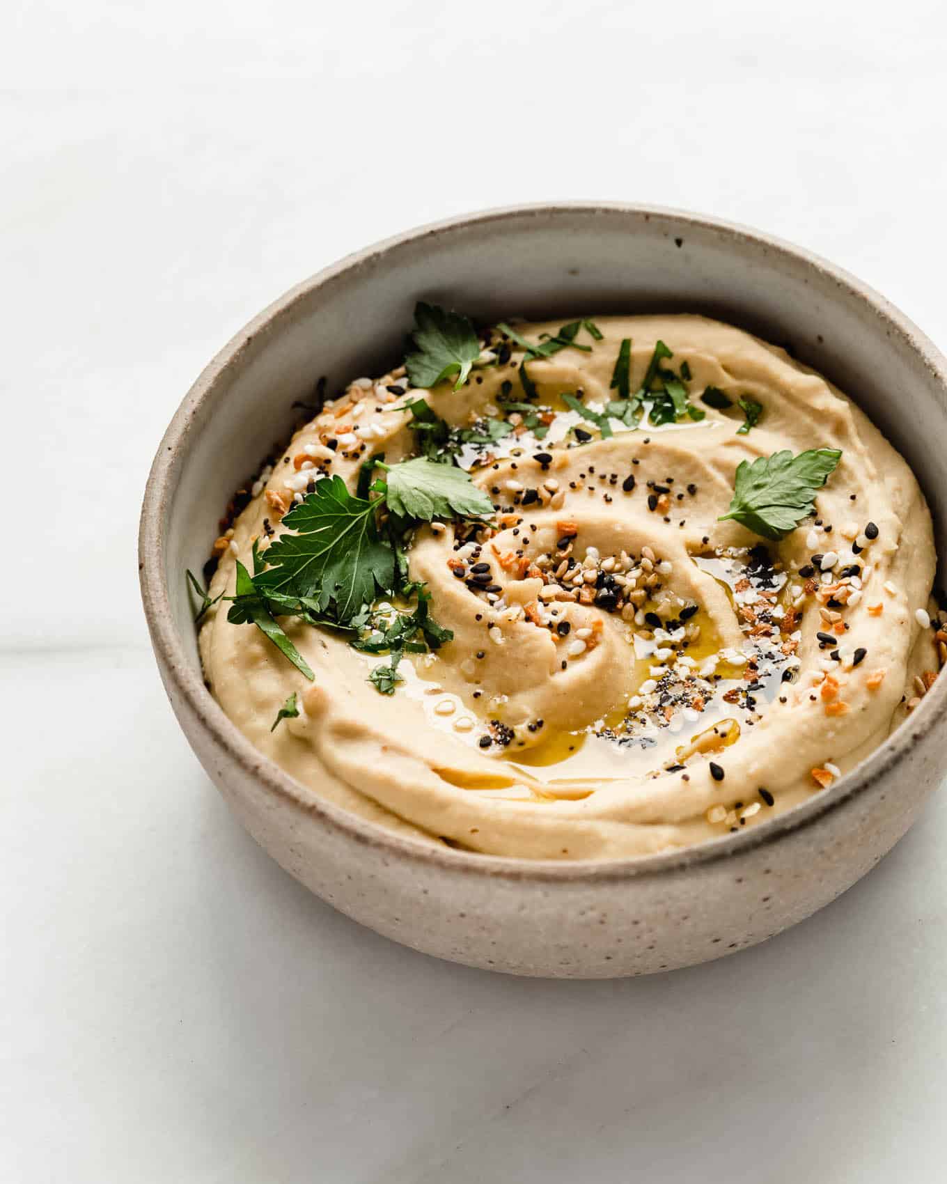 everything bagel hummus in a bowl topped with herbs.