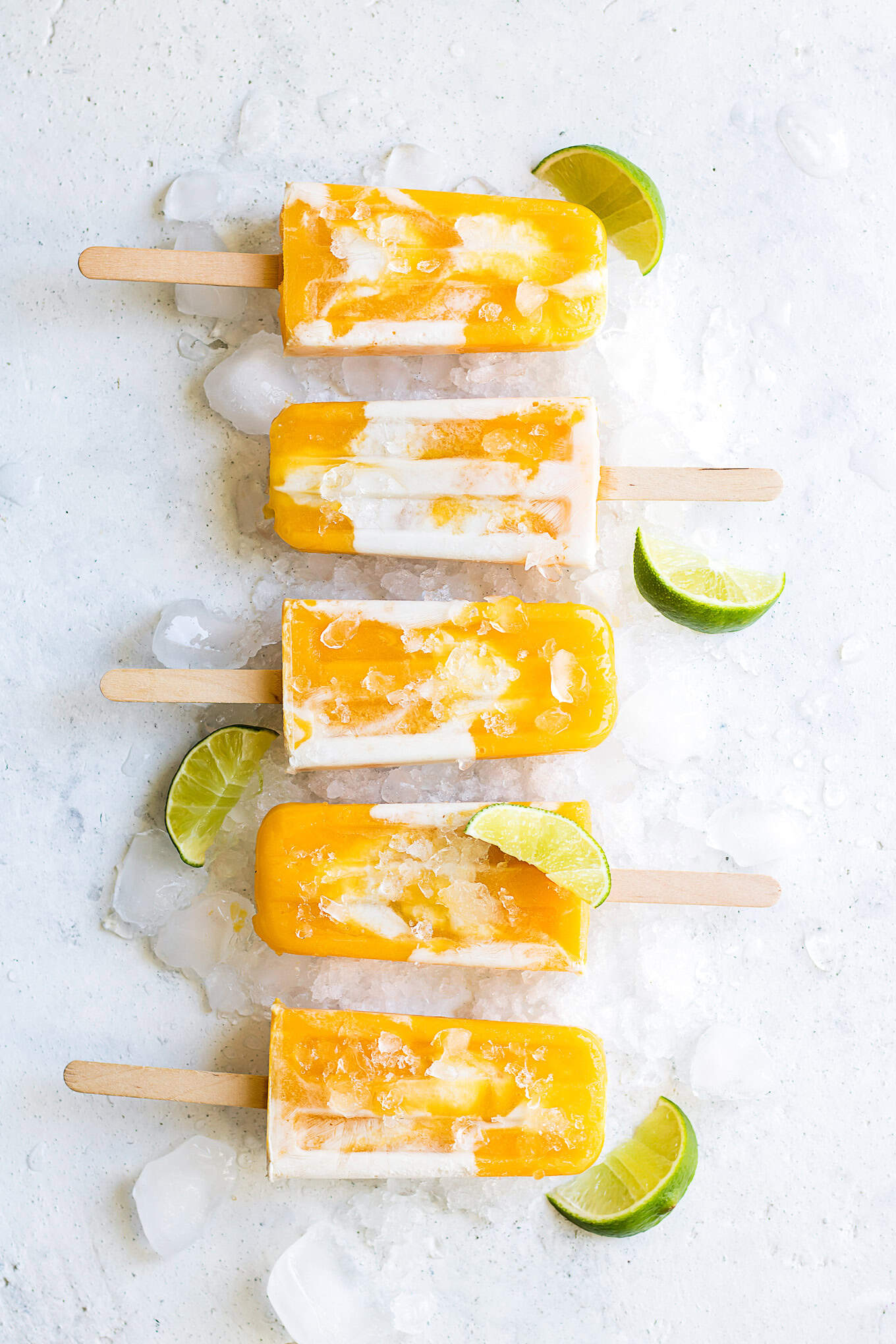 Mango popsicles lined up with limes.