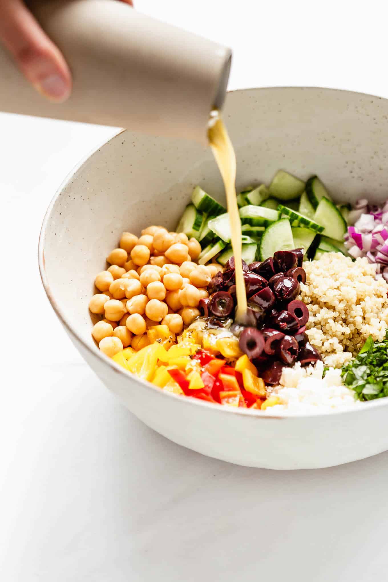 A hand pouring dressing into a bowl of quinoa salad.