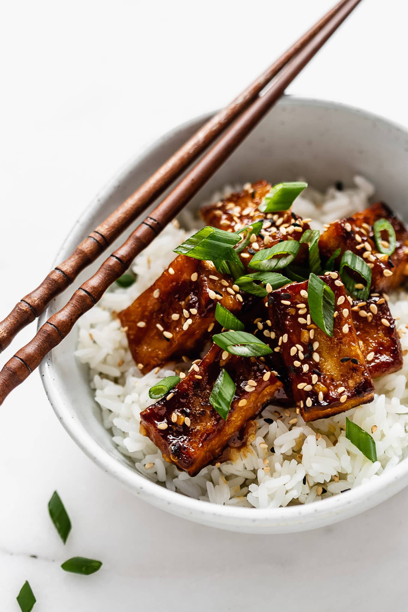 A bowl of orange tofu and rice with chopsticks