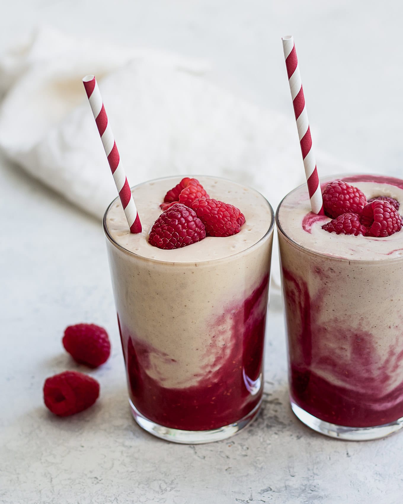 two glasses of peanut butter jelly smoothies topped with raspberries.
