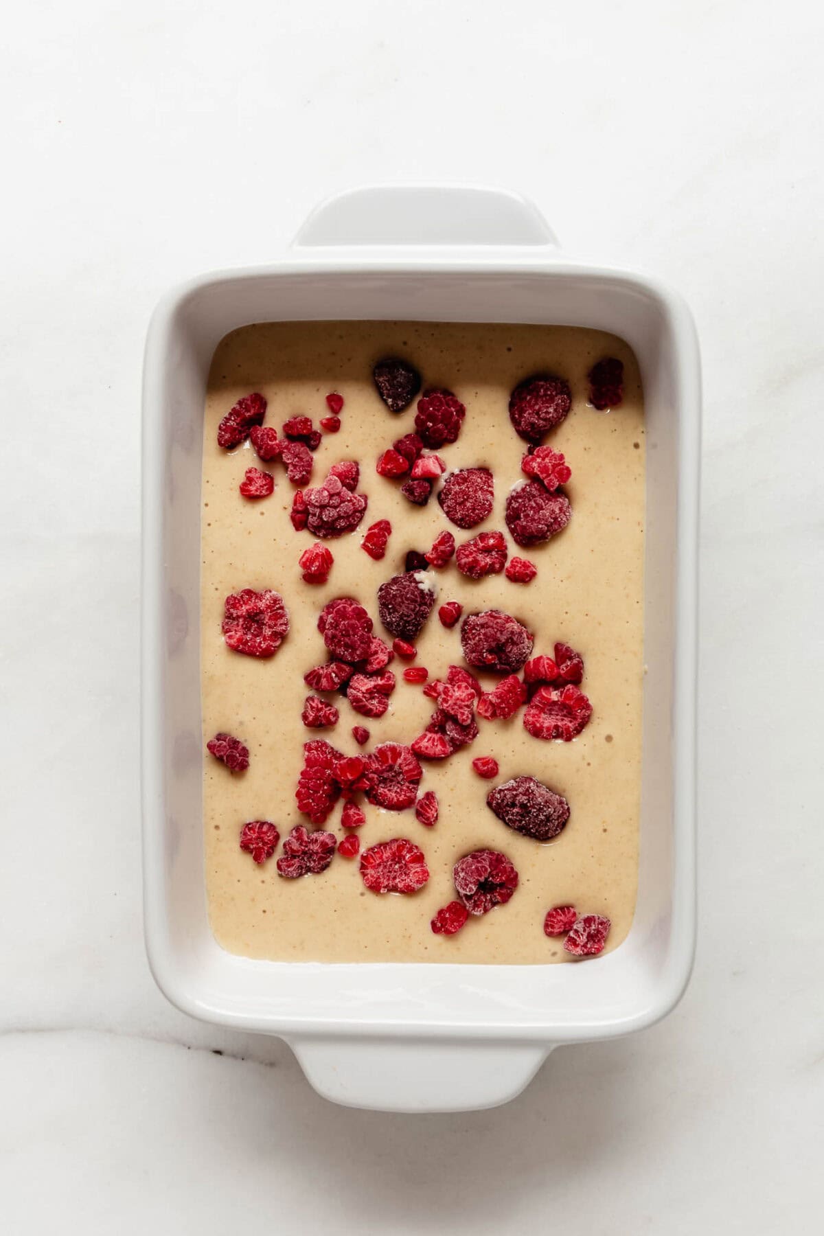 pancake bowl batter with frozen raspberries in a white baking dish