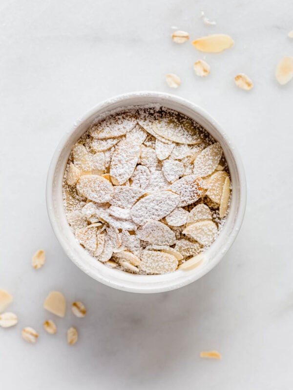 Almond croissant baked oats in a ramekin topped with sliced almonds and powdered sugar.