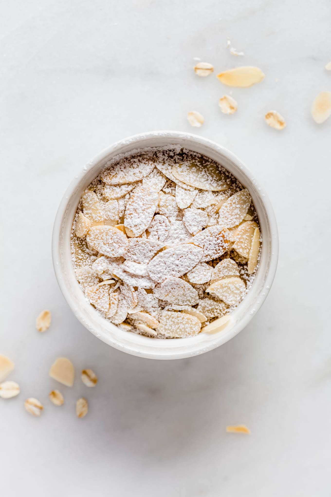 Almond croissant baked oats in a ramekin topped with sliced almonds and powdered sugar.