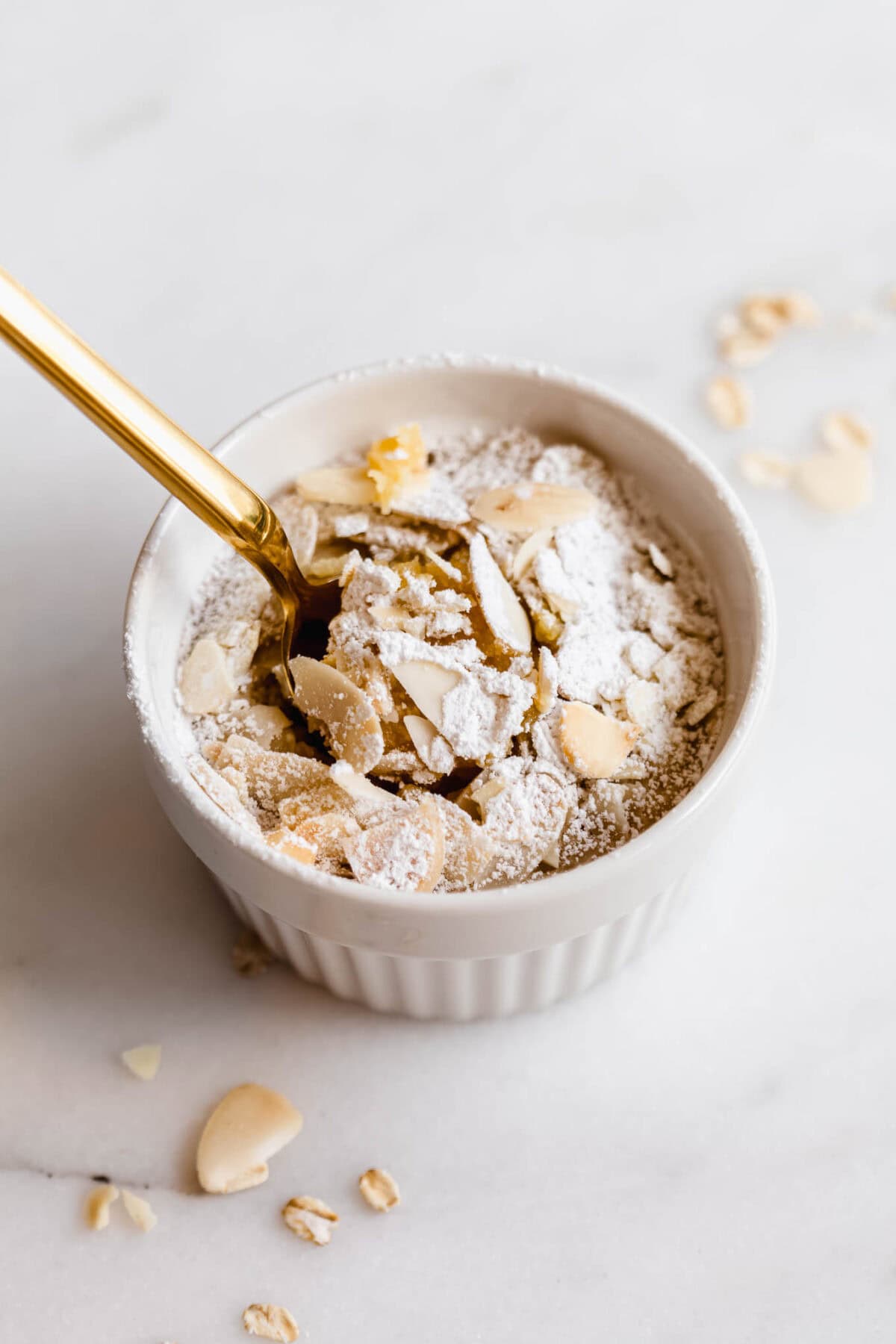 A gold spoon scooping almond baked outs out of a ramekin.