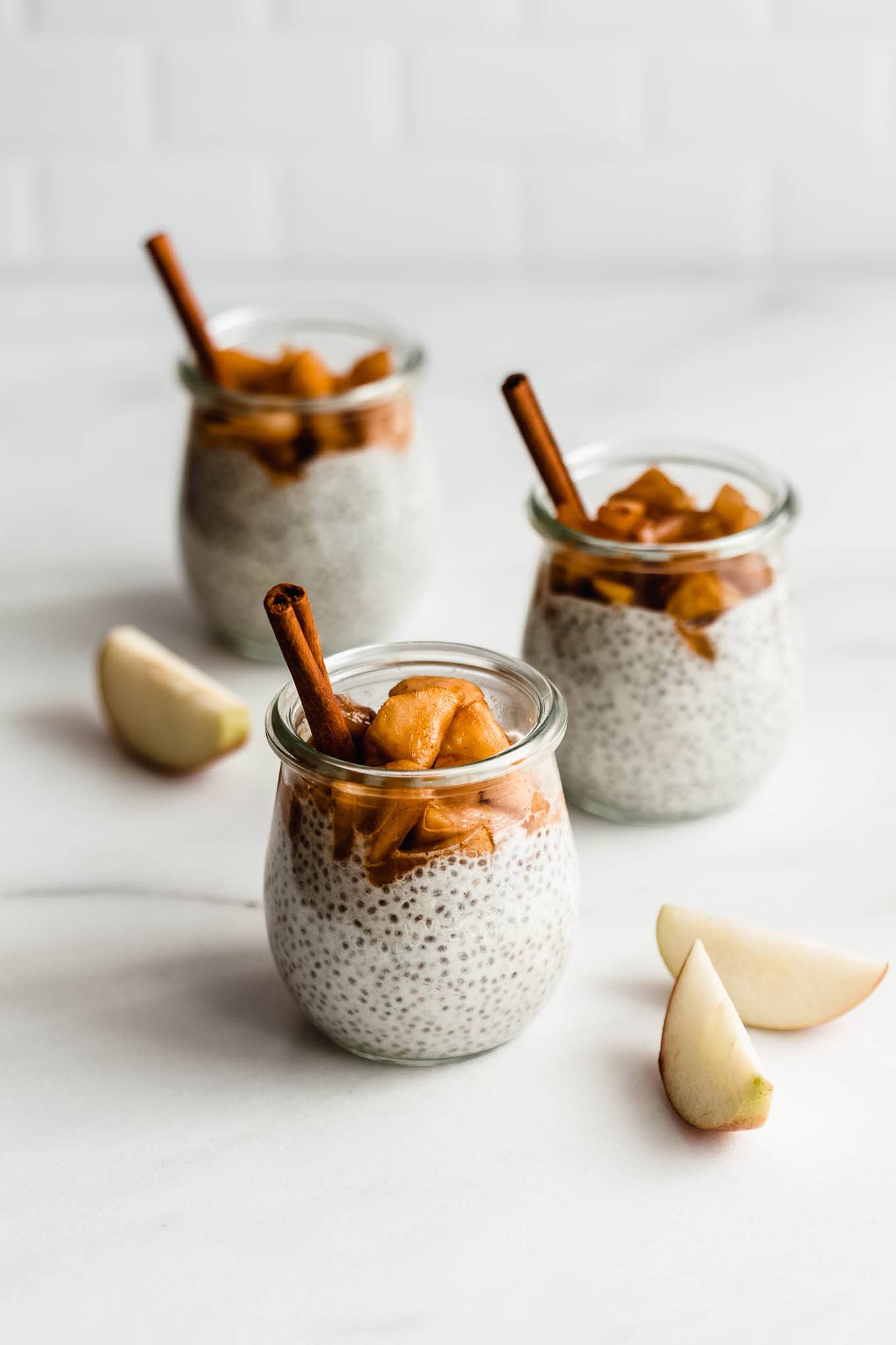 three jars of apple pie chia pudding topped with stewed apples.