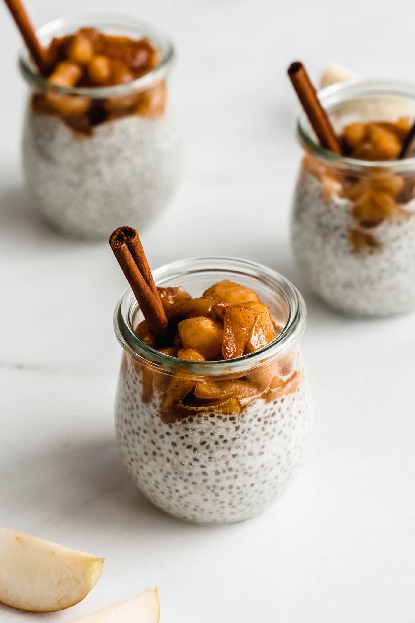 three jars of apple chia pudding topped with stewed apples.