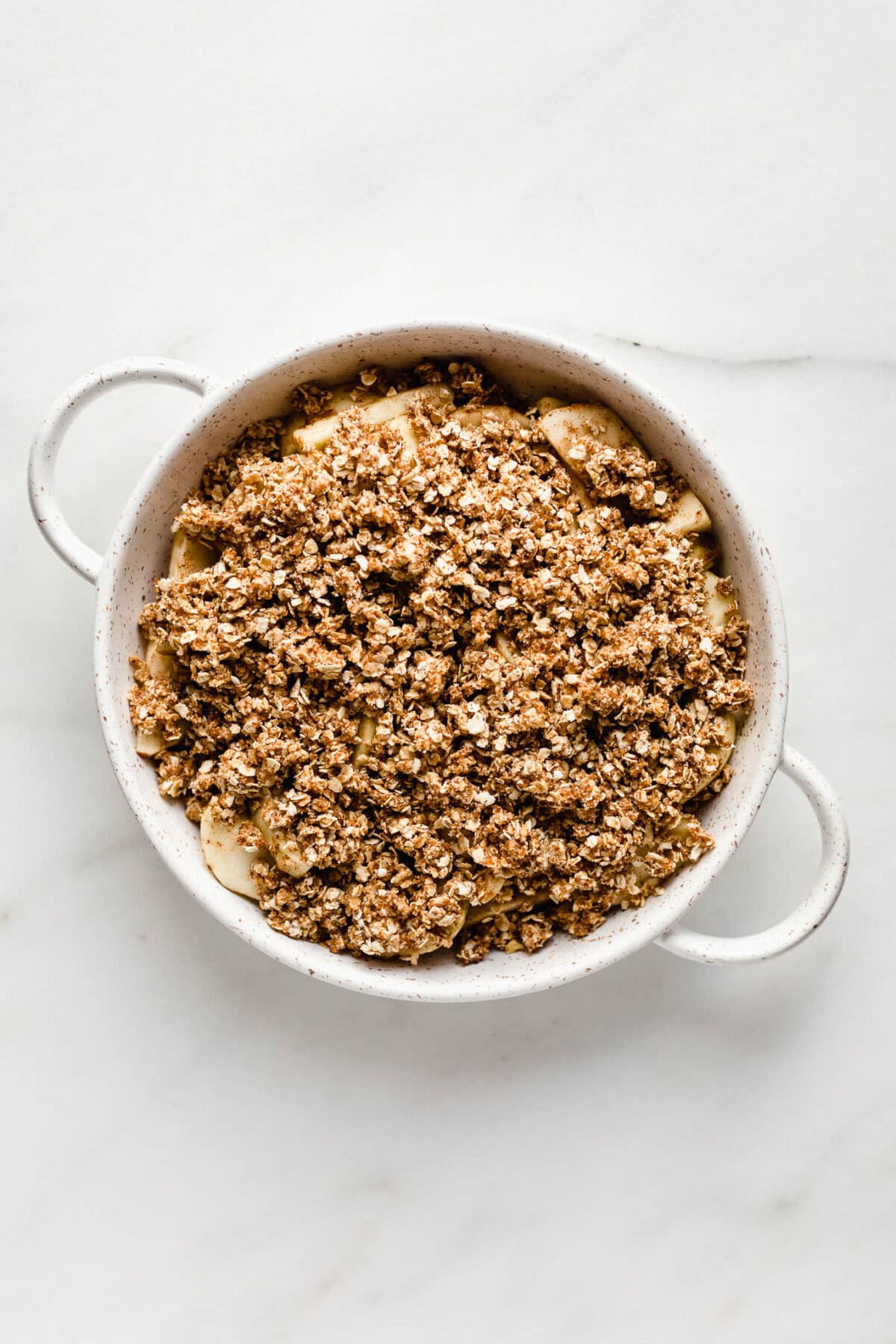 Unbaked apple crisp in a white round baking crisp.