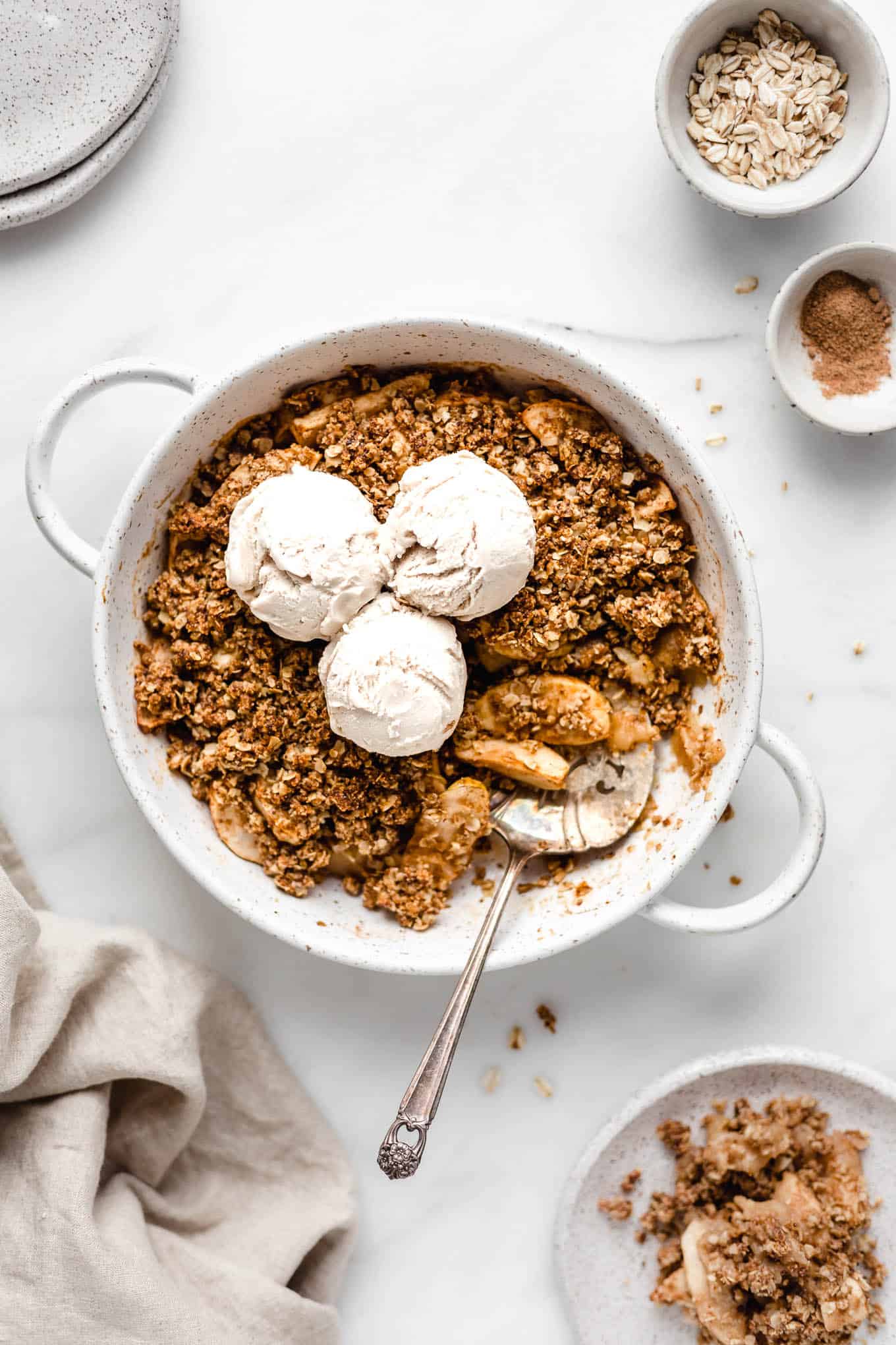 Apple crisp in a round baking dish topped with three scoops of ice cream.