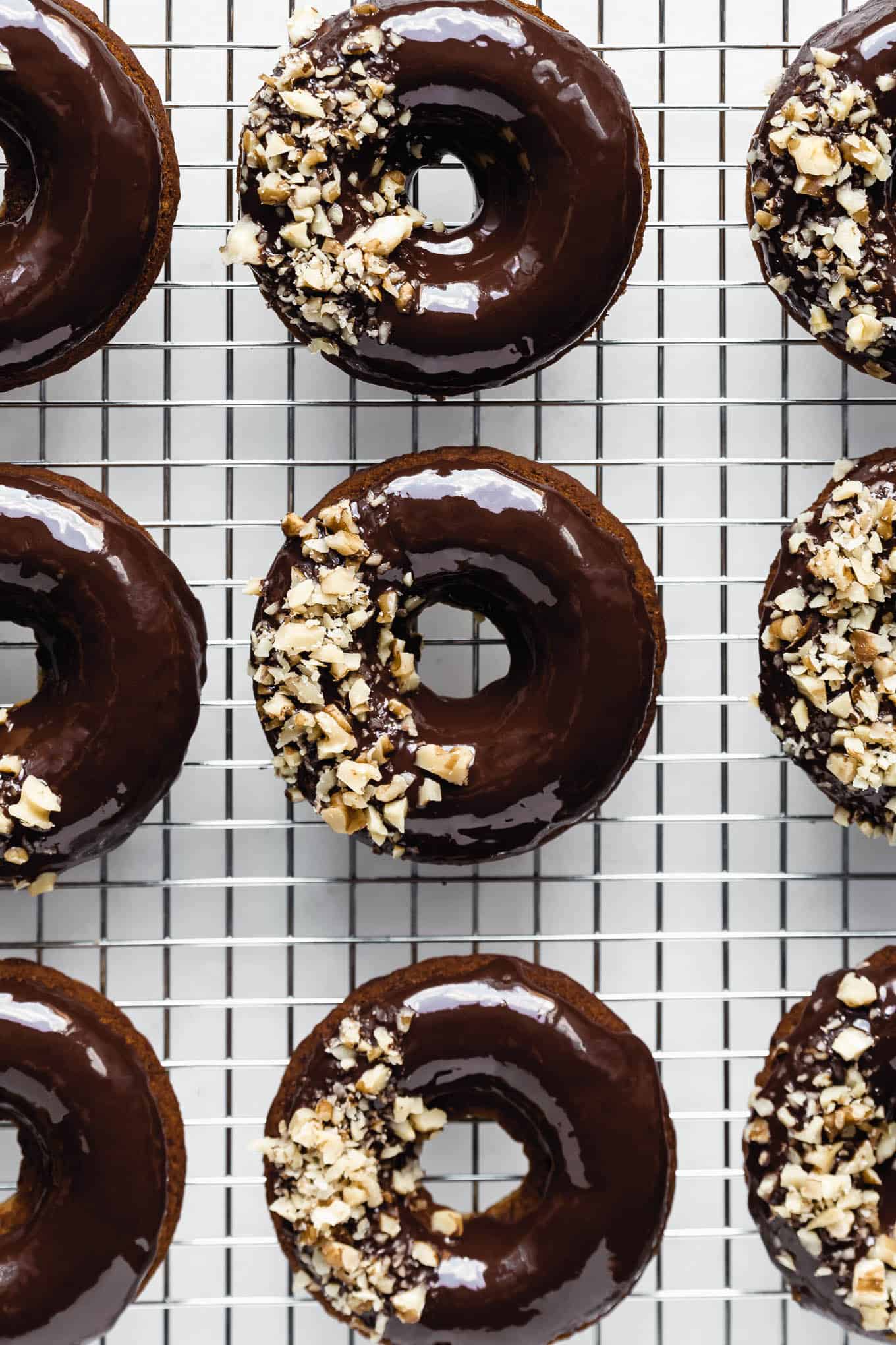 banana bread donuts on a cooling rack topped with crushed walnuts.