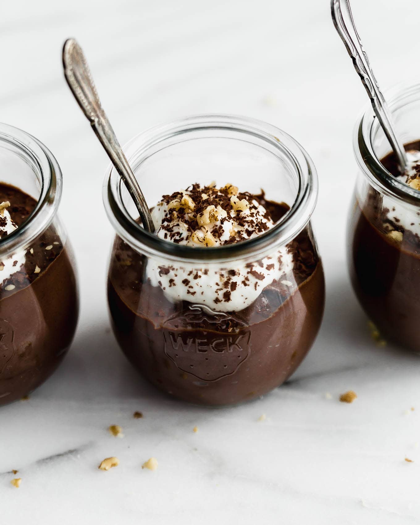 A cup of chocolate chia mousse topped with yogurt, walnuts and chocolate shavings.