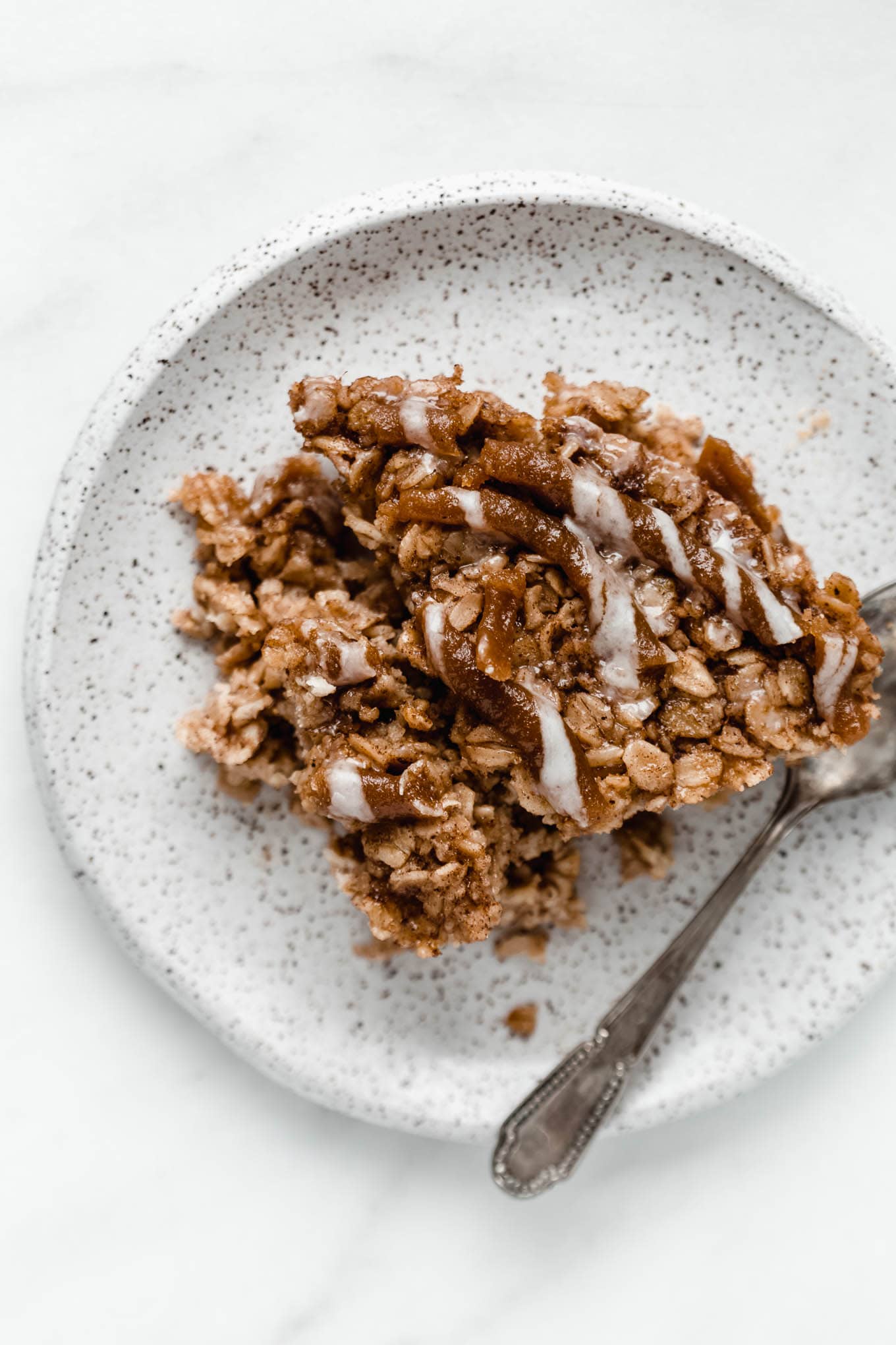 a slice of cinnamon roll baked oats on a white speckled plate.