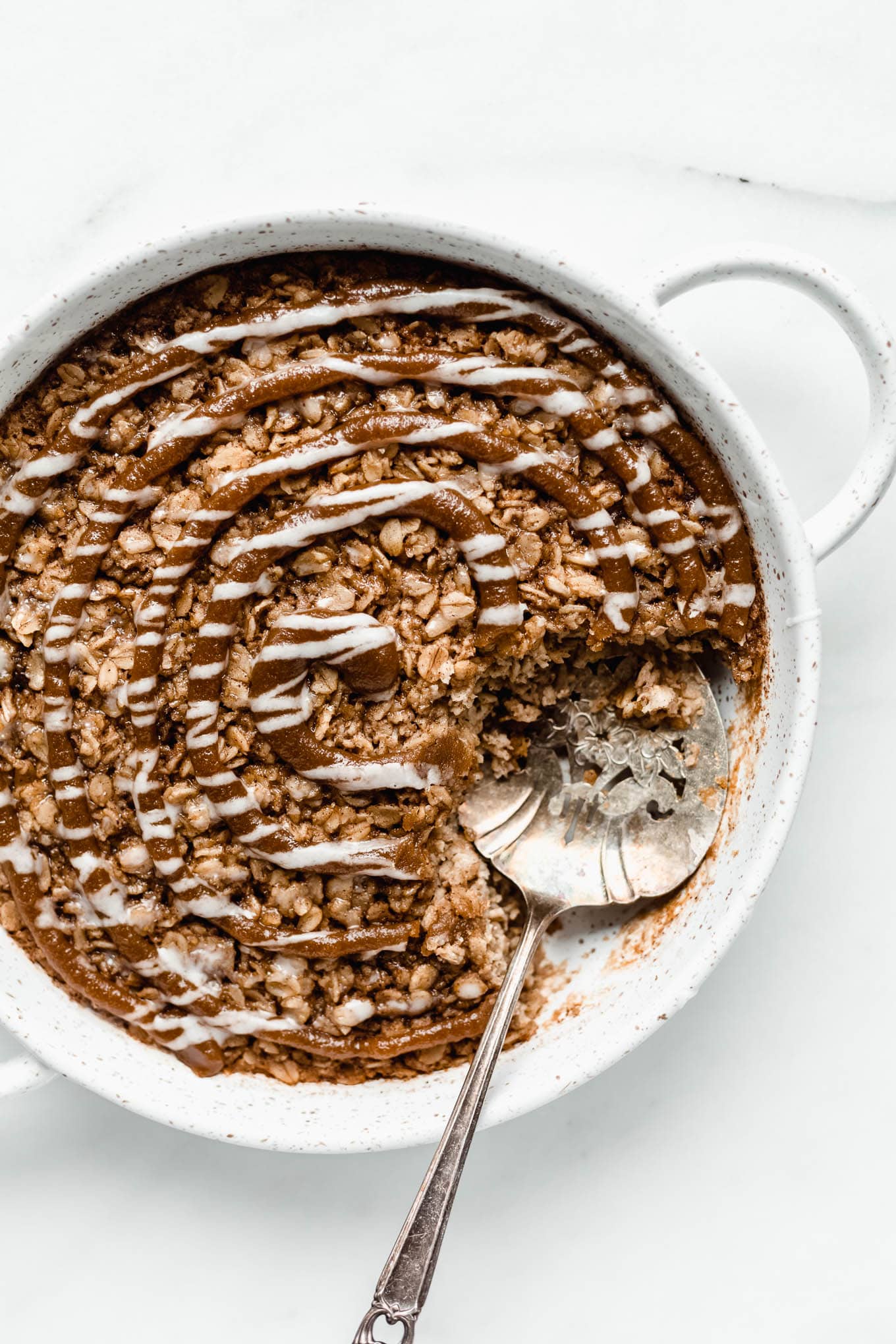 cinnamon roll baked oats in a round white baking dish with a serving spoon in it.