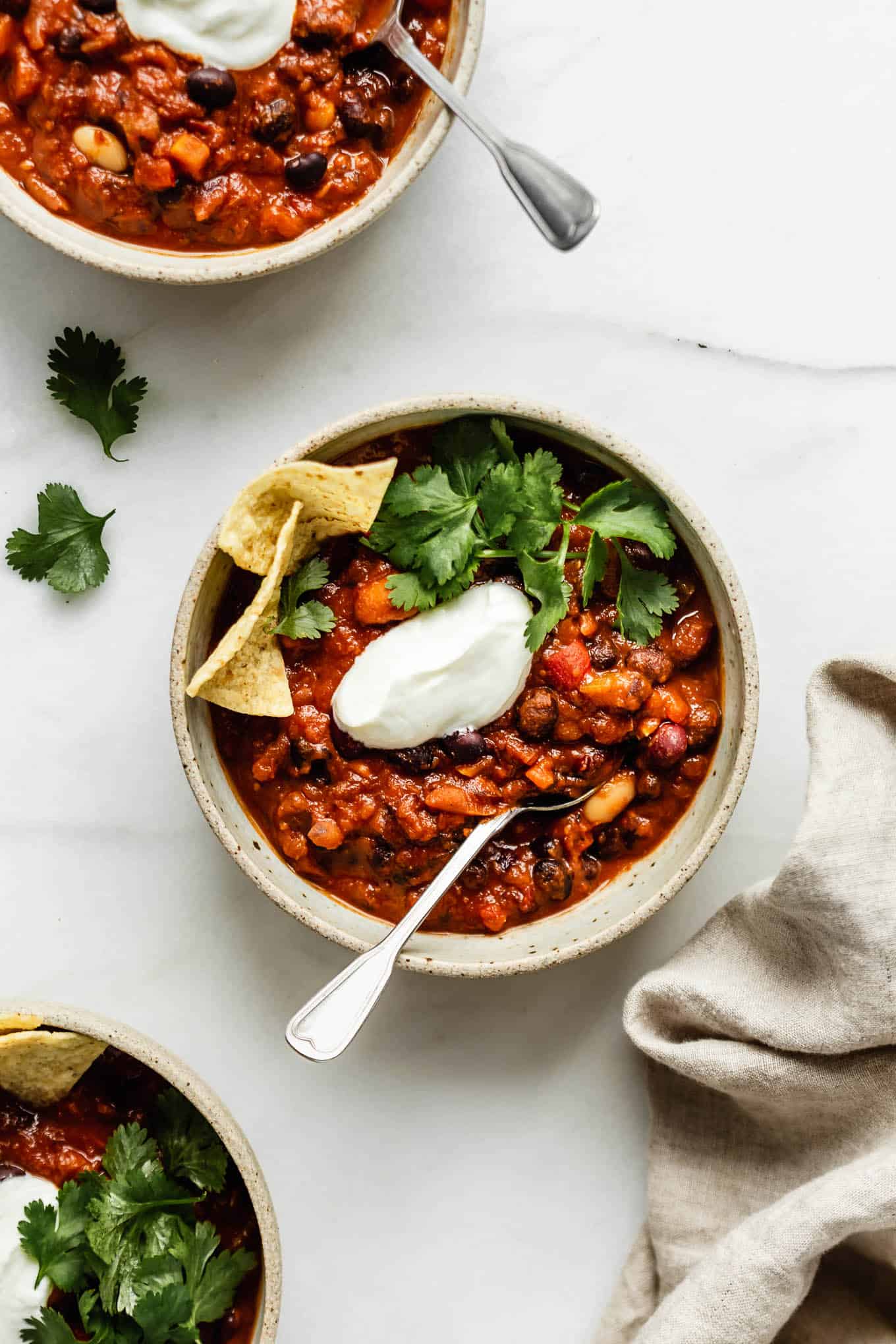 three bowls of vegan chili topped with cilantro and vegan sour cream.