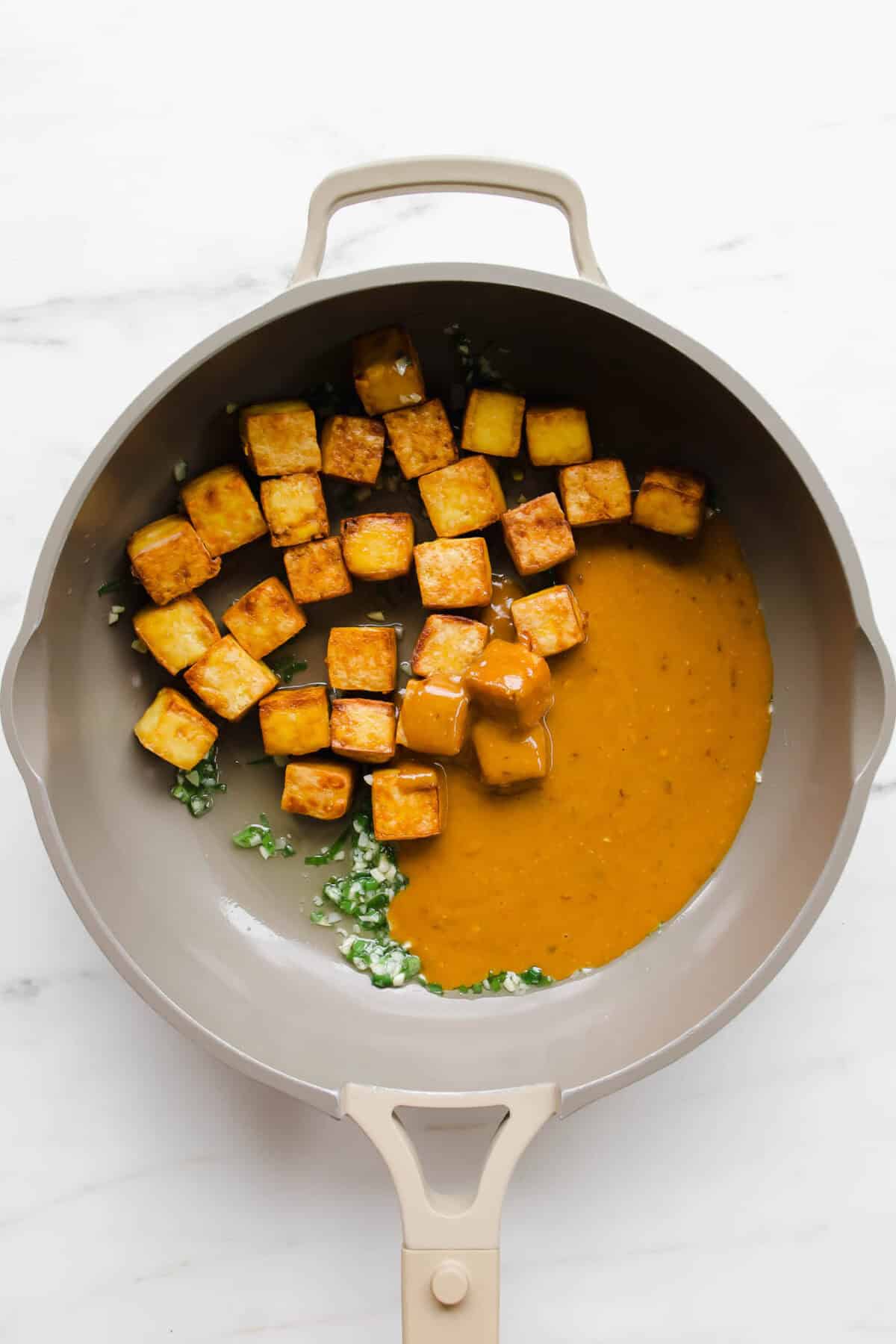 tofu cubes, chopped garlic and scallions and tofu in a taupe pan.
